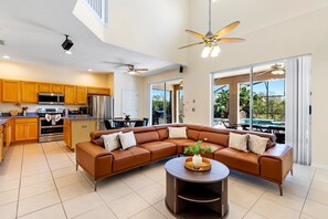 Gather comfortably in this spacious living area with plush sectional seating, flat-screen TV, and seamless flow into the modern kitchen and dining area.