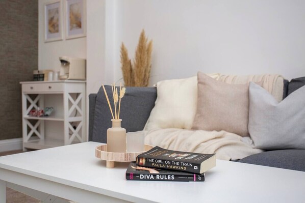 This cozy living space features a comfy sofa with soft, neutral pillows, a minimalist coffee table, and stylish decor—perfect for relaxing with a good book.