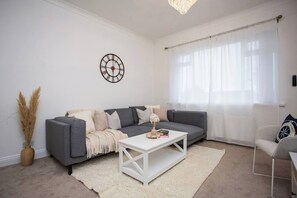This bright, inviting living room features a cozy gray sectional, soft neutral decor, and a chic coffee table. Large windows let in plenty of natural light, creating a warm and relaxing space.