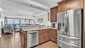 Modern kitchen with stainless steel appliances, wood cabinetry, and a view that opens into the Gulf-facing living area. Everything you need, steps from the sand.