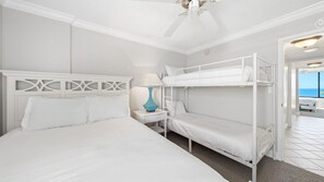 Bright and cozy guest room featuring a queen bed and twin bunk beds. Ideal for families, with a peek of the Gulf visible just down the hallway.