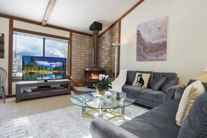 Living room with flat screen TV, wood burning fireplace, balcony access and high ceilings