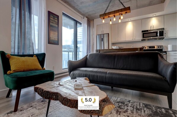 A stylish and inviting living space with a modern black leather sofa, warm lighting, and an open flow into the kitchen.