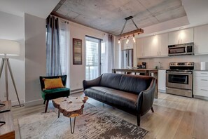 A stylish and inviting living space with a modern black leather sofa, warm lighting, and an open flow into the kitchen.