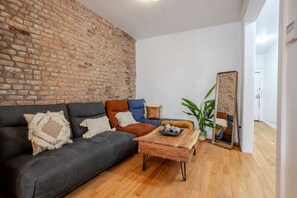 Living Room : Brick wall and leafy accents frame a cozy setup with a full-length mirror and a plush sectional