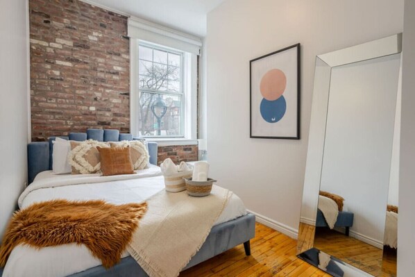 Bedroom #2: Brick feature wall, layered textures, and a full mirror create a bright and stylish retreat
