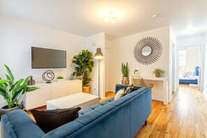 Living Room: Plush seating, Smart HD TV for streaming, and lush greenery create a cozy, inviting vibe