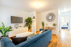 Living Room: Plush seating, Smart HD TV for streaming, and lush greenery create a cozy, inviting vibe