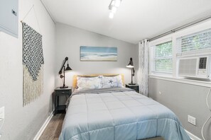 This serene bedroom features a plush queen bed, soft ocean-themed bedding, and decorative wall hangings, creating a relaxing retreat.