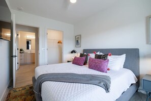 Modern and cozy bedroom features a plush bed with patterned pillows, a neutral color scheme, and ample natural lighting, creating a serene and inviting atmosphere.