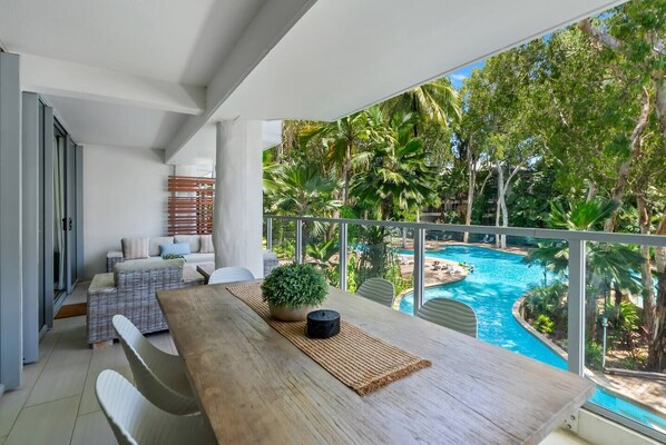 Dine alfresco on the private balcony at the six-seater table, overlooking the serene lagoon pool with a glimpse of the ocean beyond.