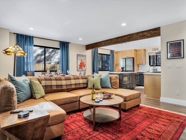 Living room w/ plush couch, in an open floor plan concept with kitchen & dining