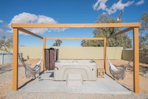 Enjoy this serene backyard with a hot tub under a wooden pergola, cozy hammocks on both sides, and a clear blue sky. Perfect for relaxation and unwinding outdoors!