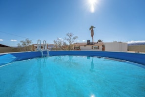 A round above-ground pool, featuring a white ladder for easy access. The beige fence and clear blue sky add to the serene atmosphere, perfect for a relaxing dip.