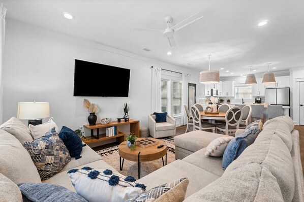 This living room features a modern, coastal-inspired design with a spacious L-shaped sectional sofa adorned with decorative pillows in neutral and blue tones.