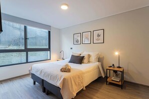 Relax in this serene bedroom featuring large windows, stylish decor, and plush bedding for a restful stay.