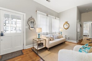 The living room at Jones Artist Boutique offers inviting seating, sunlit windows, and a smart TV—perfect for relaxing after a day of exploring Savannah.