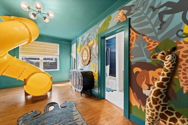The Zoo Room is where adventure meets bedtime—featuring bunk beds designed like animal cages, a jungle mural, and a slide straight from the game room!