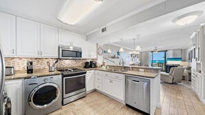This fully equipped kitchen features stainless steel appliances, granite countertops, a tile backsplash, and in-unit laundry, all set in an open layout that flows seamlessly into the living area. Enjoy ocean views while you cook, with natural light stream