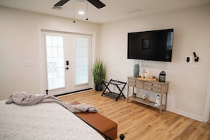Spacious primary bedroom with a mounted smart TV, stylish decor, and double doors opening to the wraparound porch—perfect for comfort and entertainment!