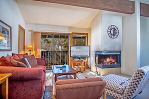 Spacious and open living area with a flat-screen TV, wood-burning fireplace, sliding glass door leading to the balcony, and a sofa sleeper that accommodates two.