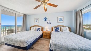 This bright and breezy guest room offers two comfortable beds adorned with nautical-themed pillows and decor. Large windows on two sides provide stunning views of the Gulf and the surrounding area, filling the space with natural light. It's the perfect co