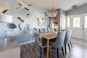 Gather around the dining table in this stylish space featuring a bold crane mural and cozy seating — perfect for shared meals or game nights
