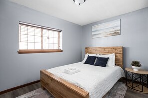 This queen bedroom features natural light, cozy decor, and a nightstand. 