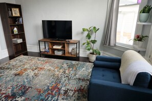 the spacious living room has a TV, bookcase, chair plants, and tall ceilings