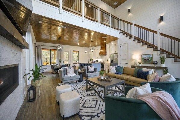 featuring a large sectional sofa, a dining table set for eight, and a staircase leading to the upper level, all accented by a rustic-chic design with wood and white shiplap walls.