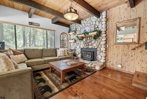 Living room with fireplace and windows looking into the pine trees.
