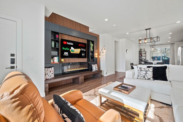 The living room Is beautiful and inviting, with the sectional and a smart TV with an electric fireplace.