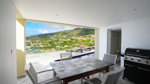 Outdoor dining area with stylish furniture, barbecue setup, and sun loungers. Perfect for alfresco meals, relaxation, and sunbathing while enjoying breathtaking ocean and mountain views. #barbecue #sunloungers #mountainview