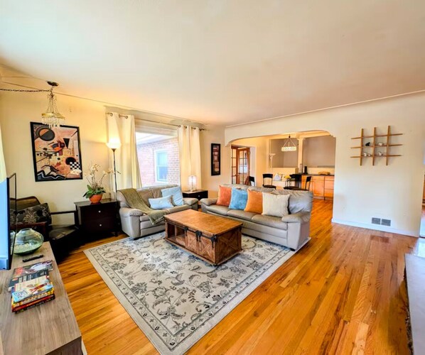Spacious, sunlit living room with comfy seating, TV, & warm hardwood floors.