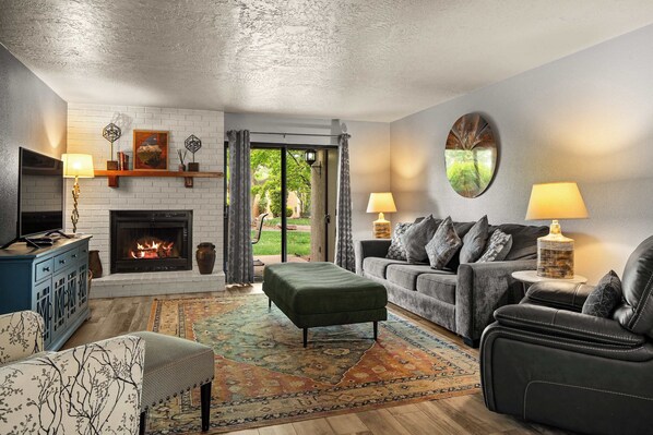 Cozy living room with a warm fireplace, stylish furniture, and a view of the lush backyard through sliding glass doors. Perfect for relaxing and entertaining!