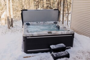 Just steps from the screen porch, immerse yourself in the warmth of the large hot tub, surrounded by the peaceful trees of our wooded lot—pure relaxation in any season.