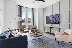 Inviting living room with a wall-mounted smart TV, a sleek leather couch, a stylish coffee table, and three accent chairs, creating a cozy and comfortable space.