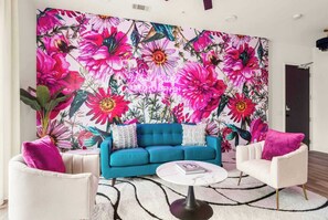 Living Room: A bright and inviting lounge area with a striking floral feature wall, cozy seating, and a neon sign for extra personality.
