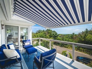 An inviting outdoor balcony with comfortable seating, sun protection from striped awnings, and a scenic view of lush greenery offers the perfect retreat.