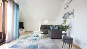 The living room boasts a large, comfortable sofa perfect for relaxation, complemented by a flat-screen TV for entertainment, creating a cozy space to unwind and enjoy your favorite shows. #modern #bright #funchal