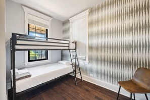Bedroom with a metal bunk bed, patterned wallpaper, a wooden chair, and a window with blinds.