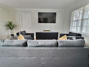 Plenty of natural light. The living area features a 65-inch Samsung Smart TV with access to Netflix and other apps (cable and streaming services not provided). Relax on the sofa and chairs with convenient drink side tables.