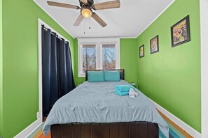Bedroom 1: Relax in this vibrant green-walled bedroom featuring a comfortable queen-sized bed, stylish decor, and natural light from large windows.