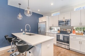The fully equipped modern kitchen features culinary essentials, stainless steel appliances, and island bar seating. (2nd Floor)