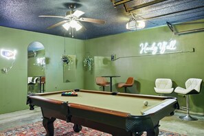 Reminiscent of vintage charm and dive bar vibes, this game room features plenty of entertainment with a pool table, bar-style tables, and stools.