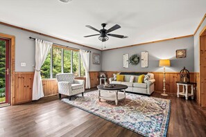 A stunning living room filled with natural light, featuring comfortable seating, warm wood paneling, and elegant decor. A peaceful retreat surrounded by the beauty of the Smoky Mountains.