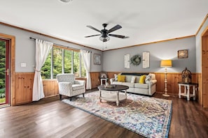 A stunning living room filled with natural light, featuring comfortable seating, warm wood paneling, and elegant decor. A peaceful retreat surrounded by the beauty of the Smoky Mountains.