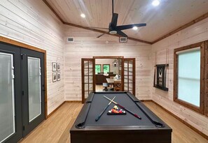 The game room is set up for endless fun, featuring a sleek pool table, stylish decor, and direct access to the rest of the cabin.