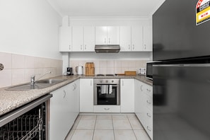 Prepare meals with ease in a bright white kitchen, equipped with modern appliances and a sleek black refrigerator.