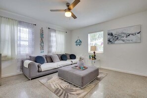 Relax in this bright and airy living room featuring beach-inspired decor, a comfortable sofa, and natural lighting from large windows.